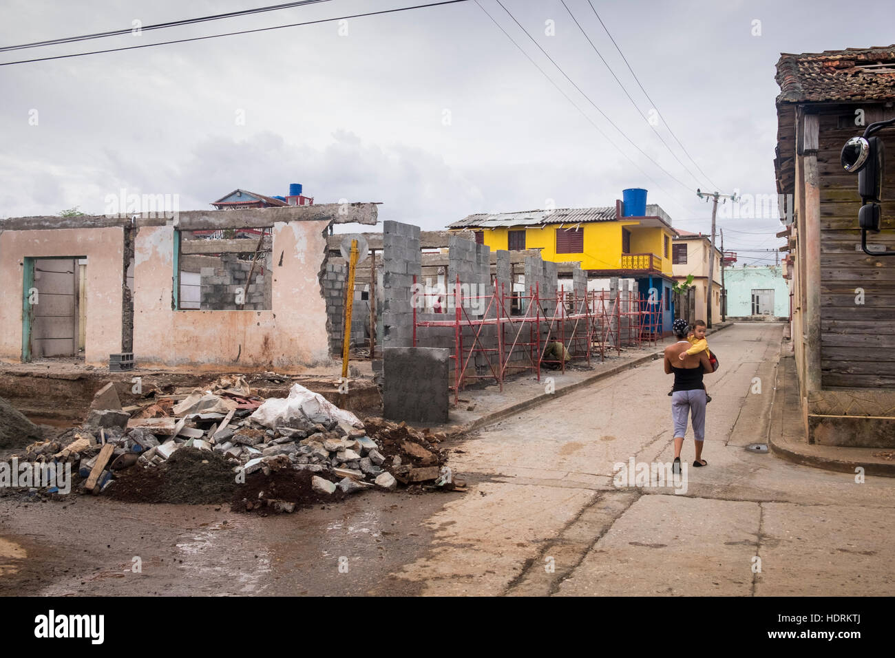 La madre e il bambino che passa attraverso la costruzione di opere di riparazione case demolite dagli effetti dell'uragano Mathew, Baracoa, Cuba Foto Stock