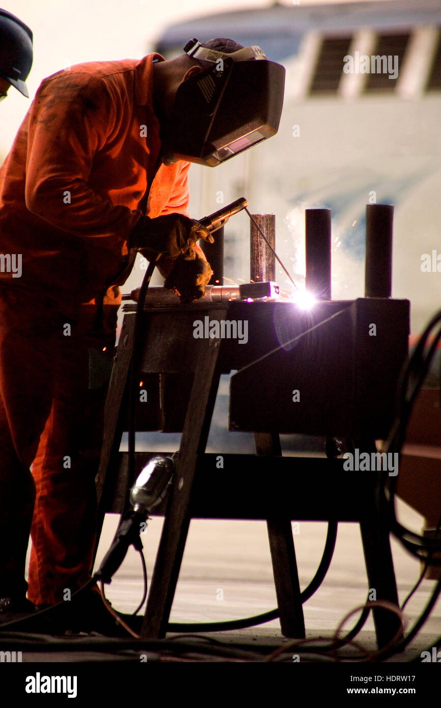 Un saldatore ad arco fa una riparazione in una Los Angeles, CA, cantiere ferroviario. Nota treno in background. Foto Stock