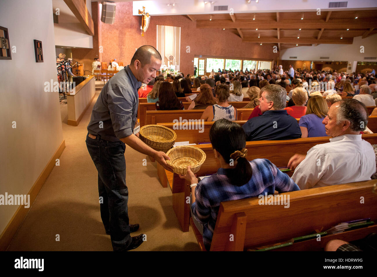 Un usciere di ispanici in una Laguna Niguel, CA, chiesa cattolica distribuisce cesti per prendere la raccolta a pomeriggio mass. Foto Stock