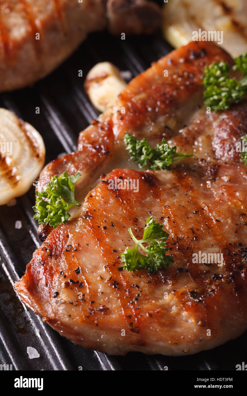 Succosa bistecca di carne di maiale alla griglia con cipolle e aglio in una padella grill macro. In verticale Foto Stock