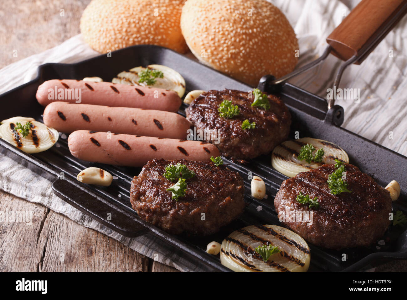 Hamburger e salsicce con verdure su una padella per grigliare closeup. orizzontale Foto Stock