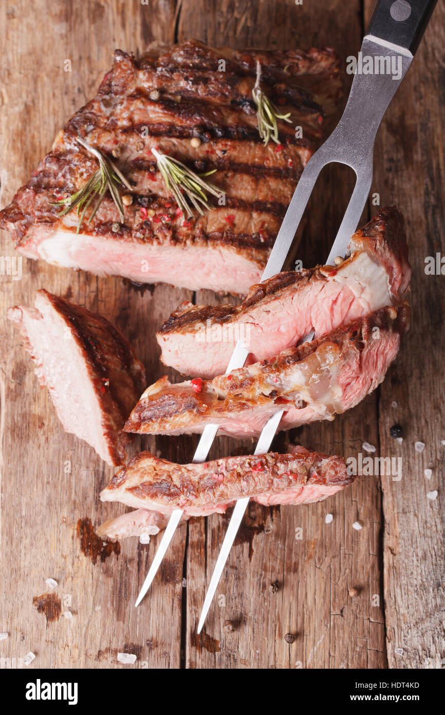 Tagliate a fette grigliate di carne di manzo con una forcella per la carne. verticale vista superiore Foto Stock