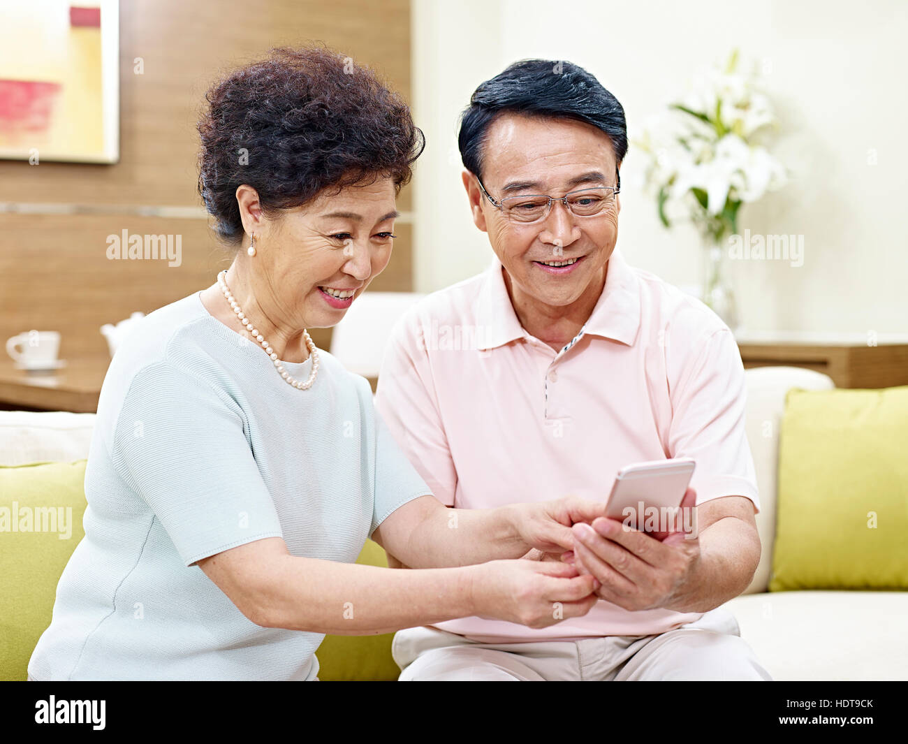 Senior asian giovane seduto sul divano guardando al cellulare insieme, felice e sorridente Foto Stock