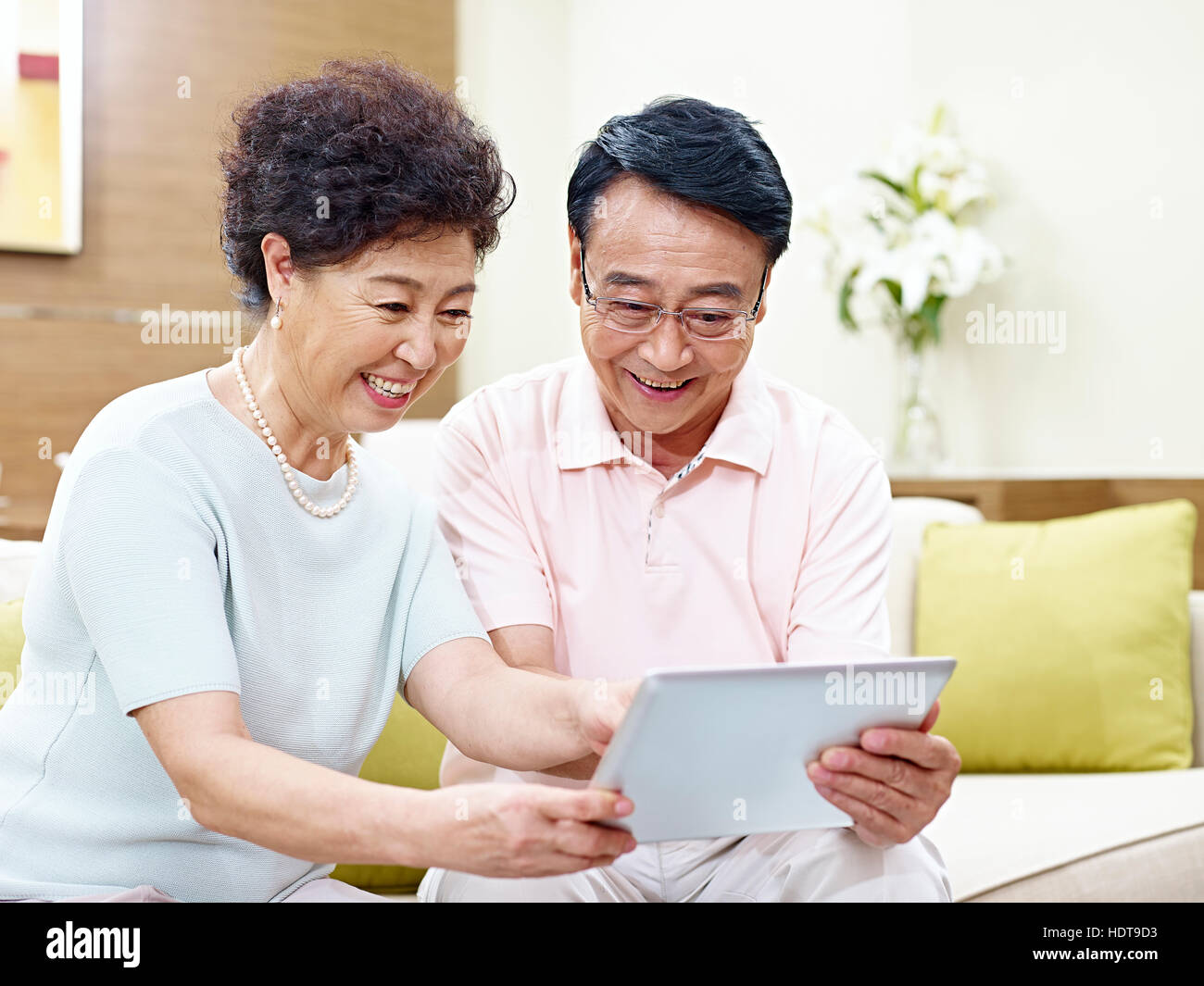 Senior asian giovane seduto sul divano guardando al computer tablet insieme, felice e sorridente Foto Stock