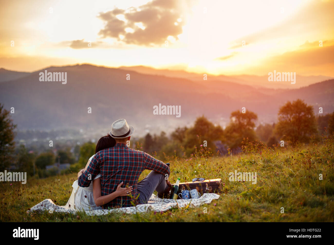 Felice di amare giovane seduto su plaid in campo. sullo sfondo delle montagne. Foto Stock