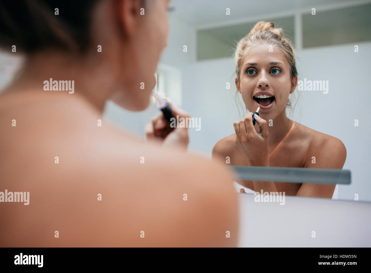 La riflessione della donna nello specchio mentre si applica il trucco sulla sua faccia. Femmina caucasica mettendo il rossetto in bagno. Foto Stock