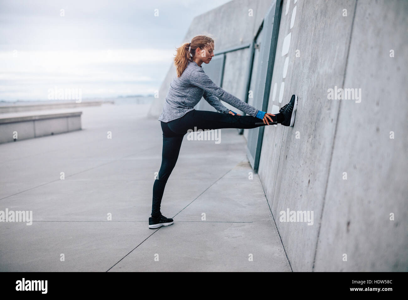 Vista laterale colpo di giovane donna fitness stretching all'esterno. Femmina gambe stretching contro la parete. Foto Stock