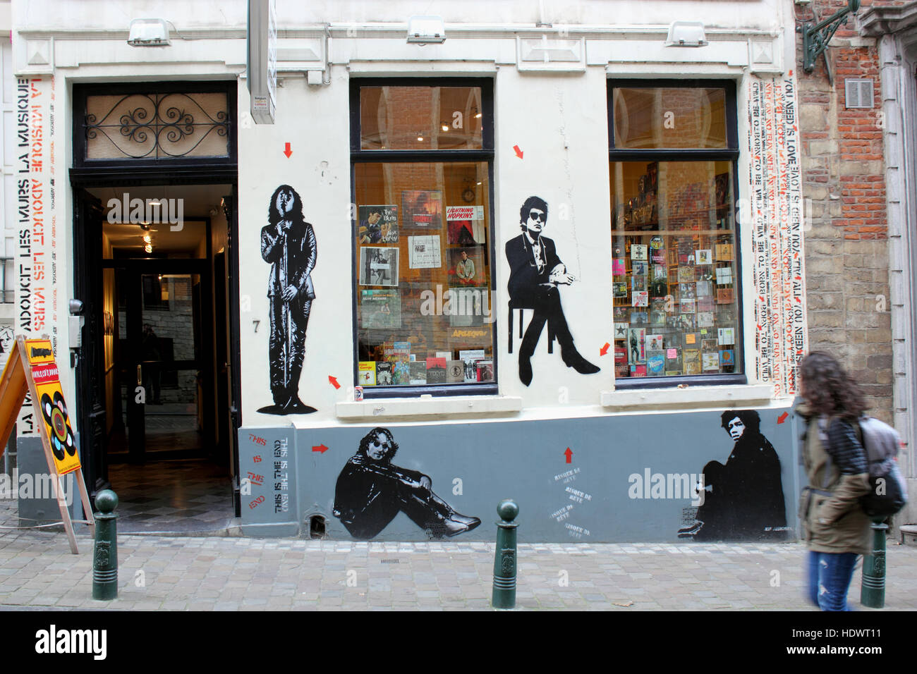 Ragazza camminare passato negozio di musica in Bruxelles con murali di Lennon, Dylan e Hendrix Foto Stock