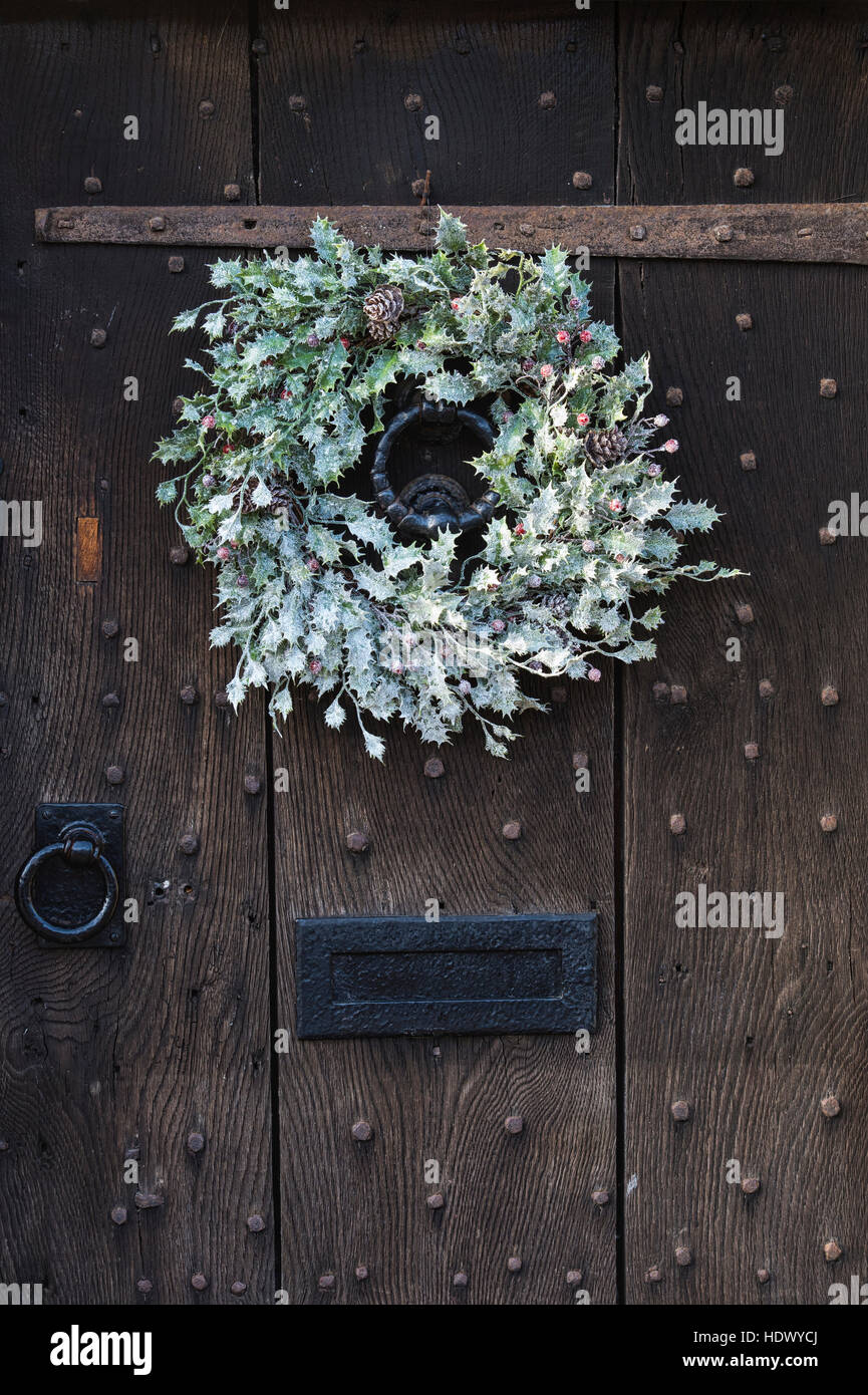 Bianco Natale holly corona sulla vecchia quercia legno chiodati porta. Cotswolds, Inghilterra Foto Stock