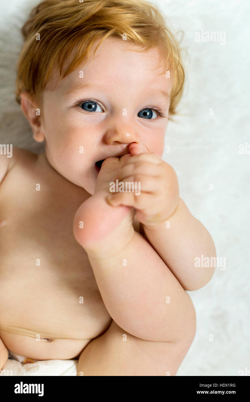 Caucasian baby boy mordere il piede Foto Stock