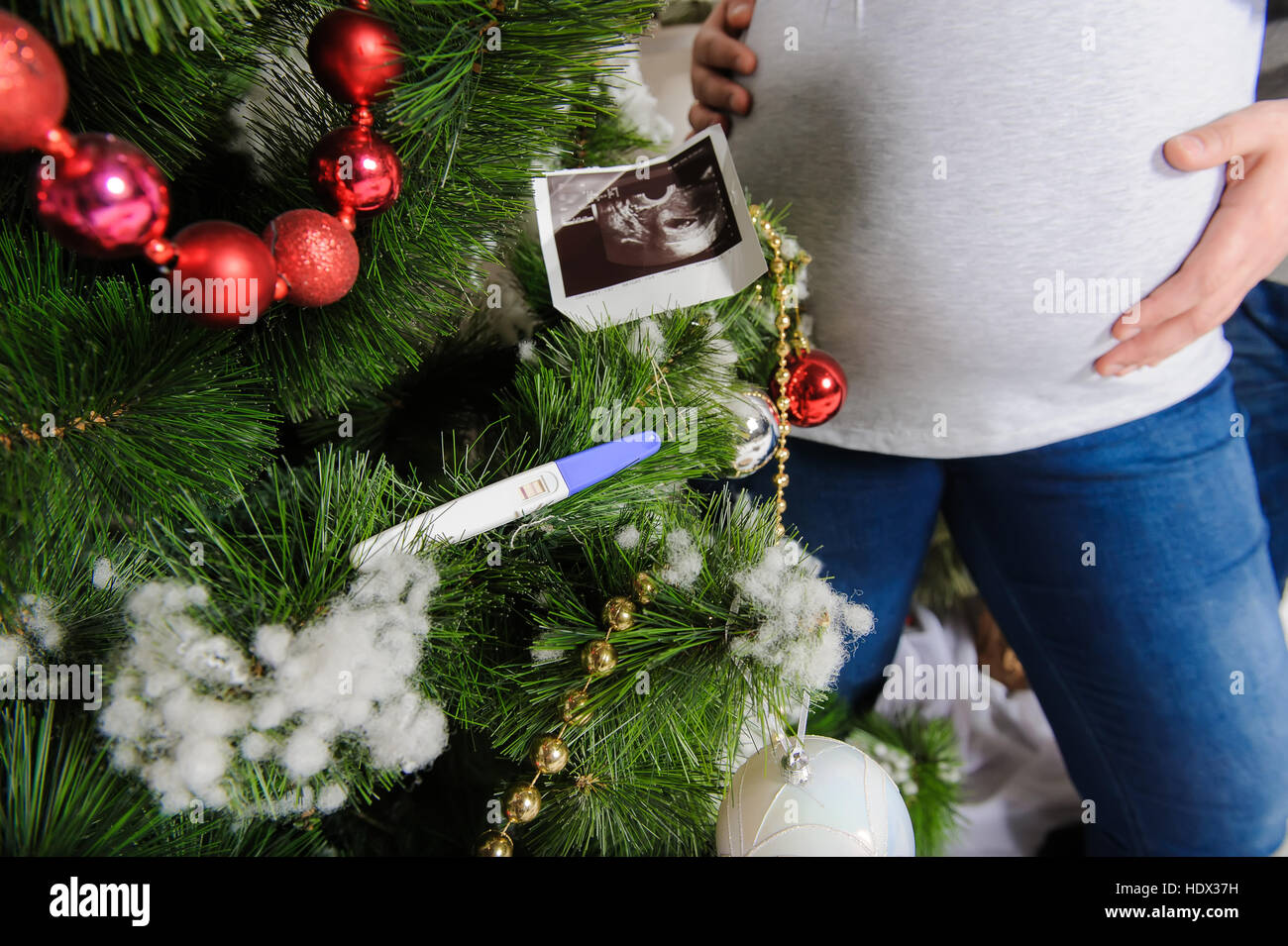 Immagine ad ultrasuoni del bambino, test di gravidanza su albero di Natale.  Incinta giovane nei pressi di un albero di Natale. Il marito abbracciando  la sua moglie incinta Foto stock - Alamy