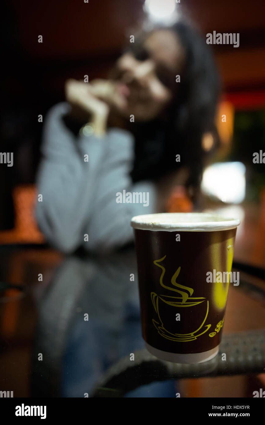 Una ragazza di sfocatura dello sfondo con una tazza di caffè nel fuoco anteriore, tazza di caffè stampati su di essa Foto Stock