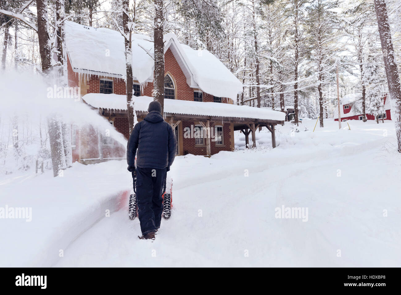 Uomo con un ventilatore di neve l'eliminazione di un vialetto di una casa in una bella innevato paesaggio invernale di Muskoka, Ontario, Canada Foto Stock