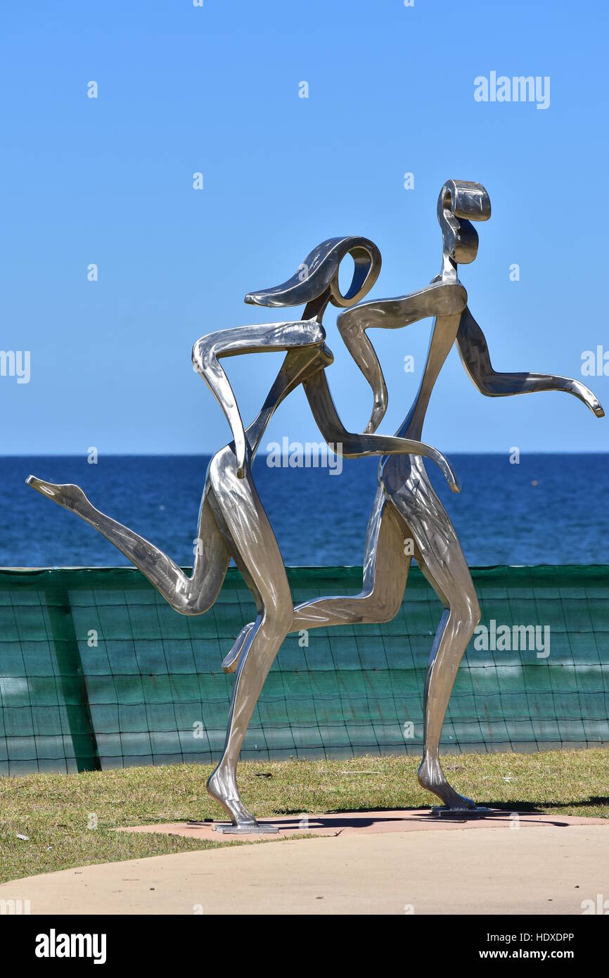 Lucido metallo in lega di scultura di maschi e femmine di jogging lungo la spiaggia dell'oceano in Gold Coast. Foto Stock
