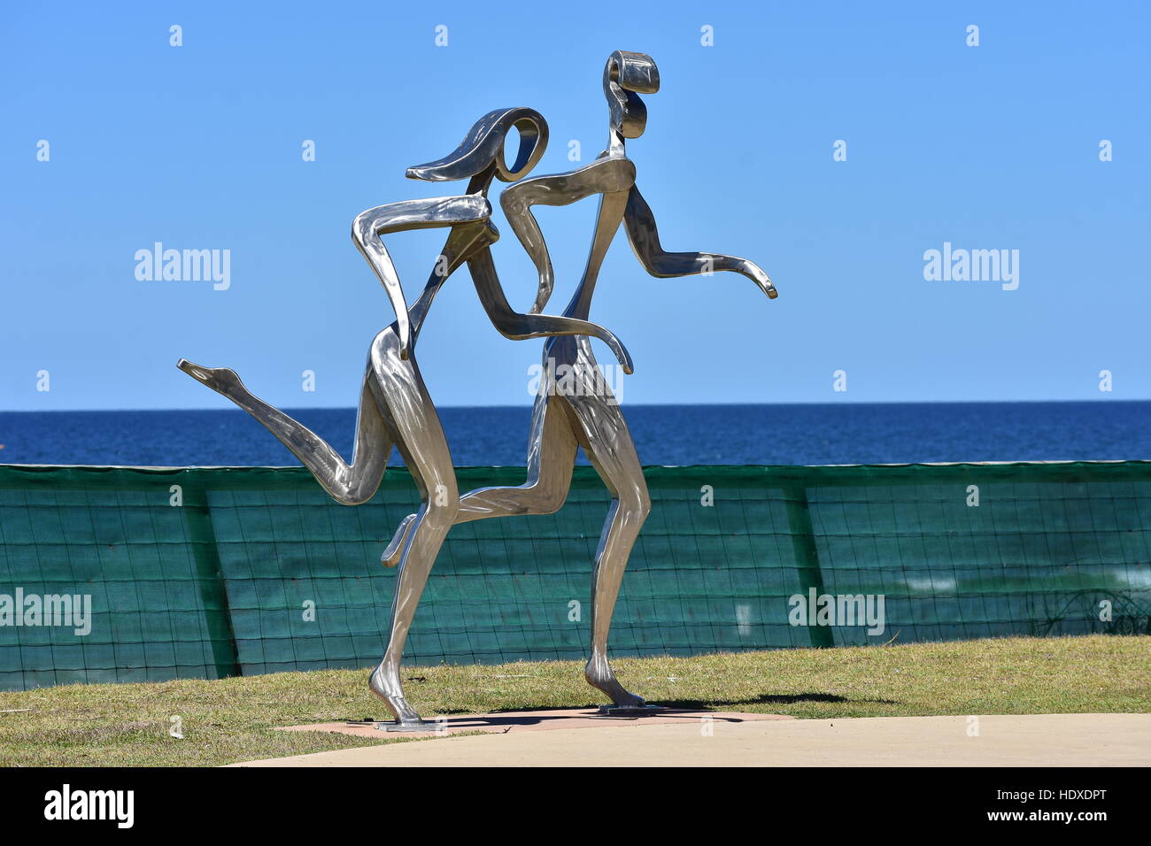 Lucido metallo in lega di scultura di maschi e femmine di jogging lungo la spiaggia dell'oceano in Gold Coast. Foto Stock