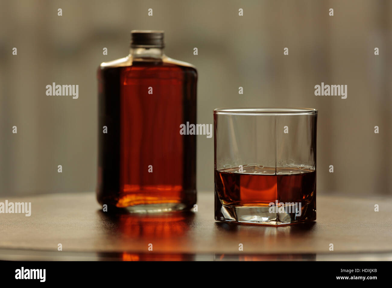 Bottiglia e bicchiere di whisky insieme sulla pelle e tavolo di mogano Foto Stock