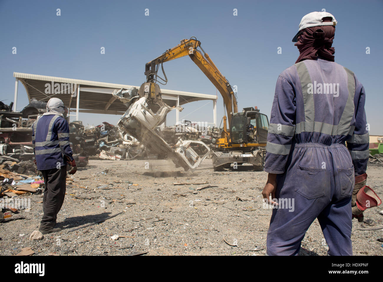 I lavoratori migranti guarda come una vettura viene schiacciata in corrispondenza di un deposito di riciclaggio, gli Emirati arabi uniti Foto Stock
