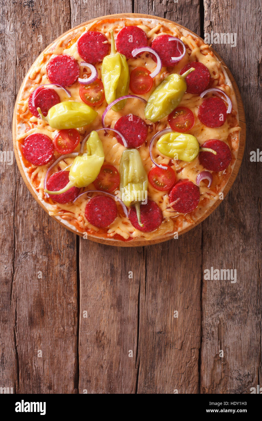 La pizza italiana con salame e salsiccia per pizza pepe e pomodori in una tabella di close-up vista verticale dal di sopra, stile rustico Foto Stock