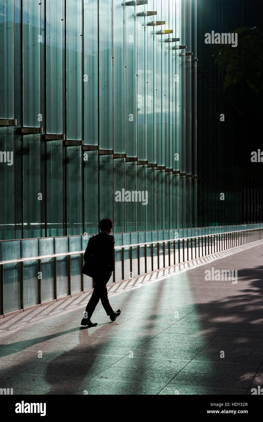 Silhouette di un salarista che cammina sul fronte di vetro di un alto edificio di uffici a Shiodome, Shimbashi, Tokyo, Giappone. Foto Stock
