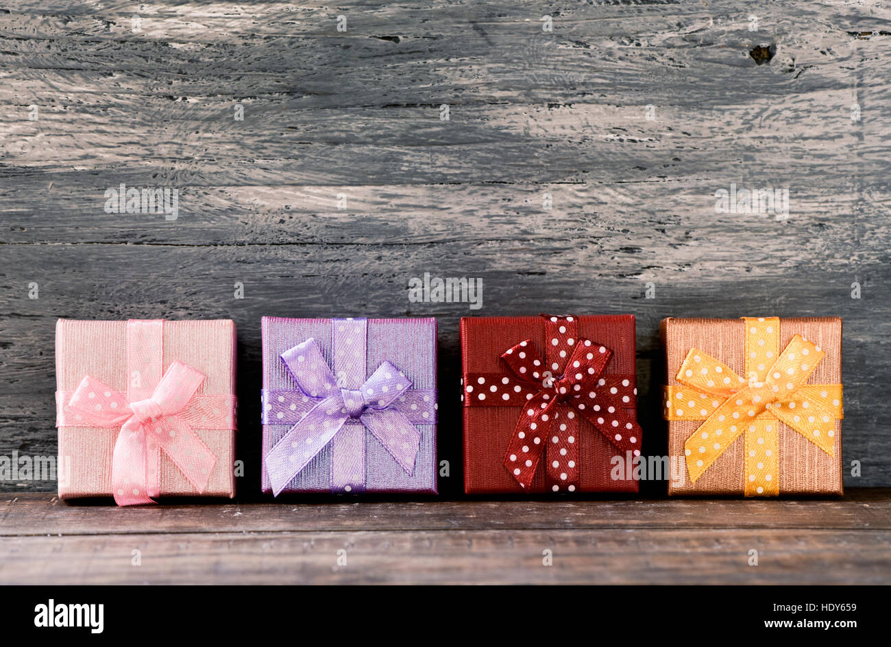 Alcuni doni accogliente avvolto in diversi documenti e legato con nastri di diversi colori disposti in linea su un rustico di una superficie di legno, con un negativo spa Foto Stock