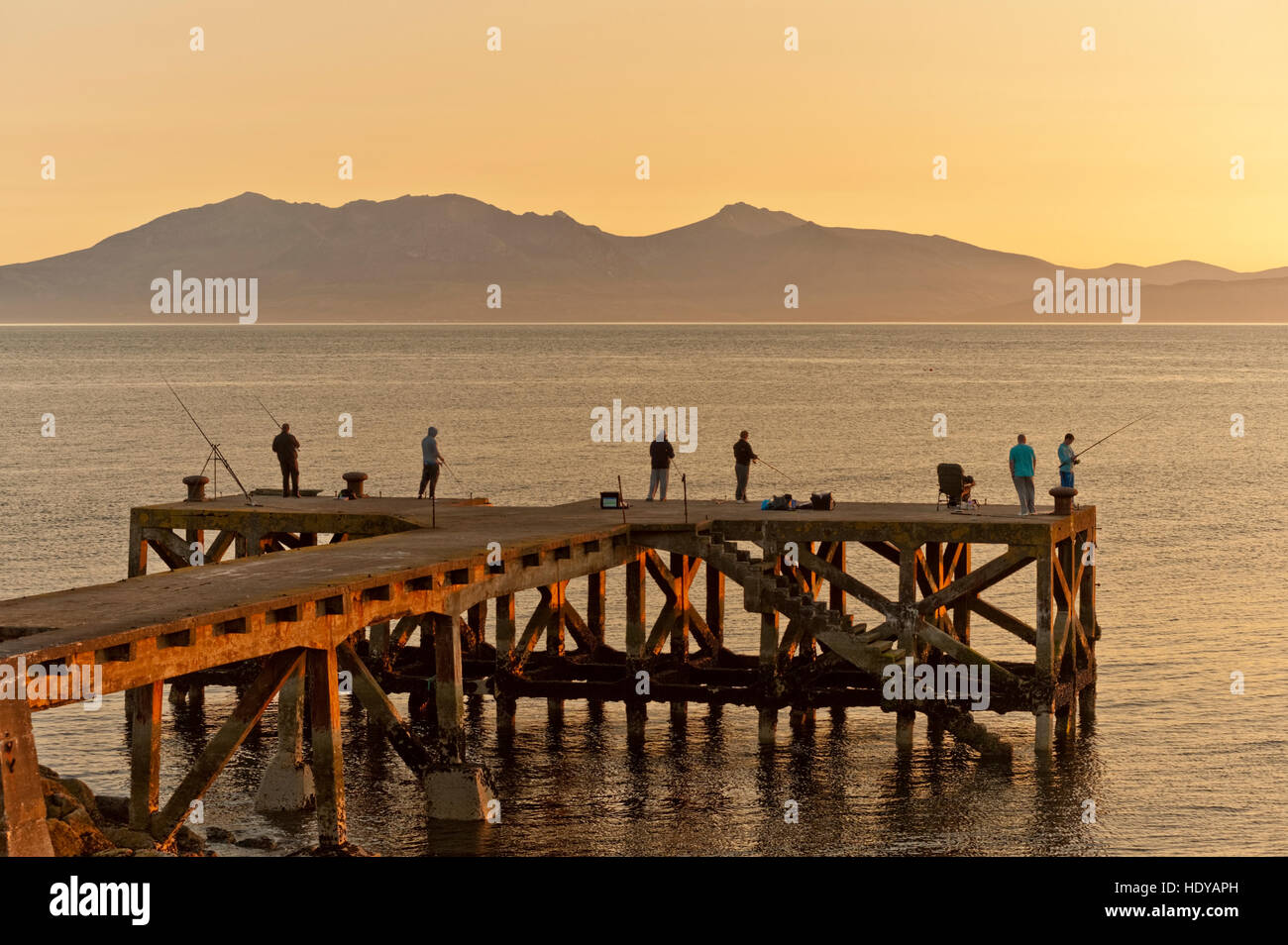 I pescatori del mare nel vecchio molo Portencross al tramonto con le colline di Aran dietro. Foto Stock