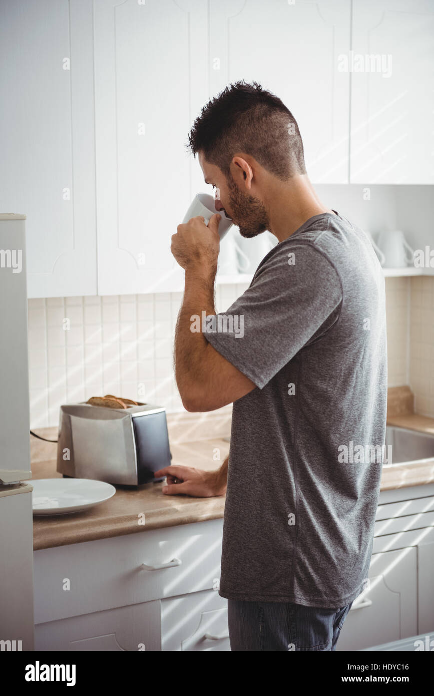 L uomo come tostare il pane per la colazione e di bere il caffè in cucina Foto Stock
