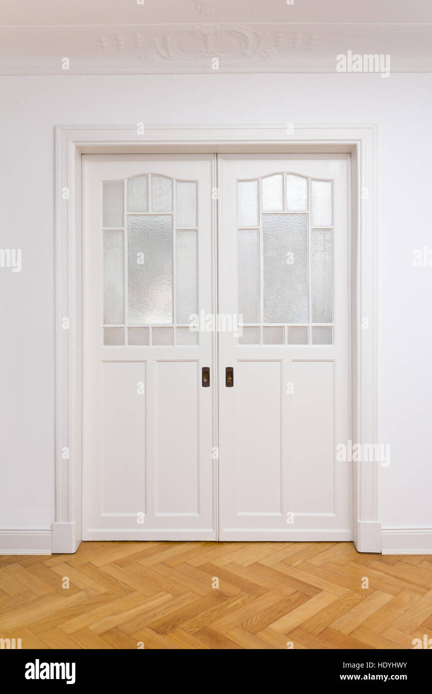 Vecchio bianco doppia porta scorrevole con vetro testurizzato in un edificio storico con pavimentazione in parquet di rovere, copia o spazio di testo Foto Stock