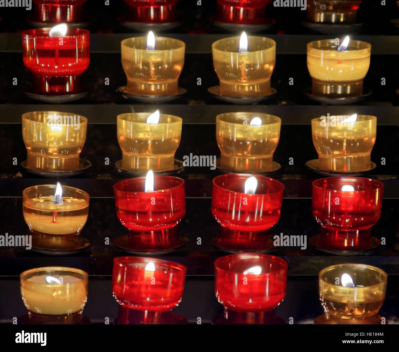 Serie di acceso candele votive collocate all'interno di piccoli vetri colorati in bicchieri di rosso e giallo e collocati su scaffali in legno in una chiesa Foto Stock