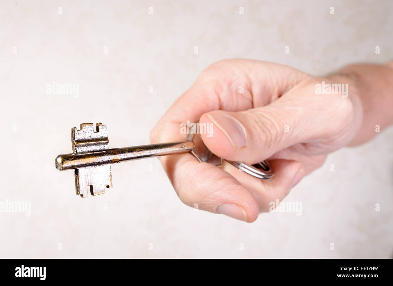 Una mano d'uomo è in possesso di una chiave di apertura o chiusura di una porta, su sfondo chiaro Foto Stock