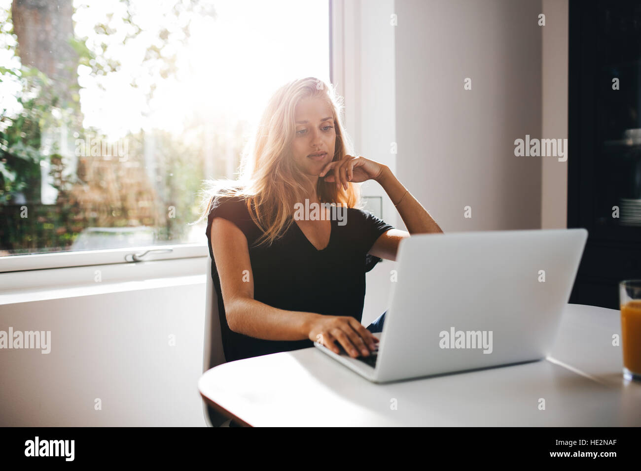Giovane donna rilassante in cucina e utilizzando laptop. Lavoro femminile sul portatile a casa. Foto Stock