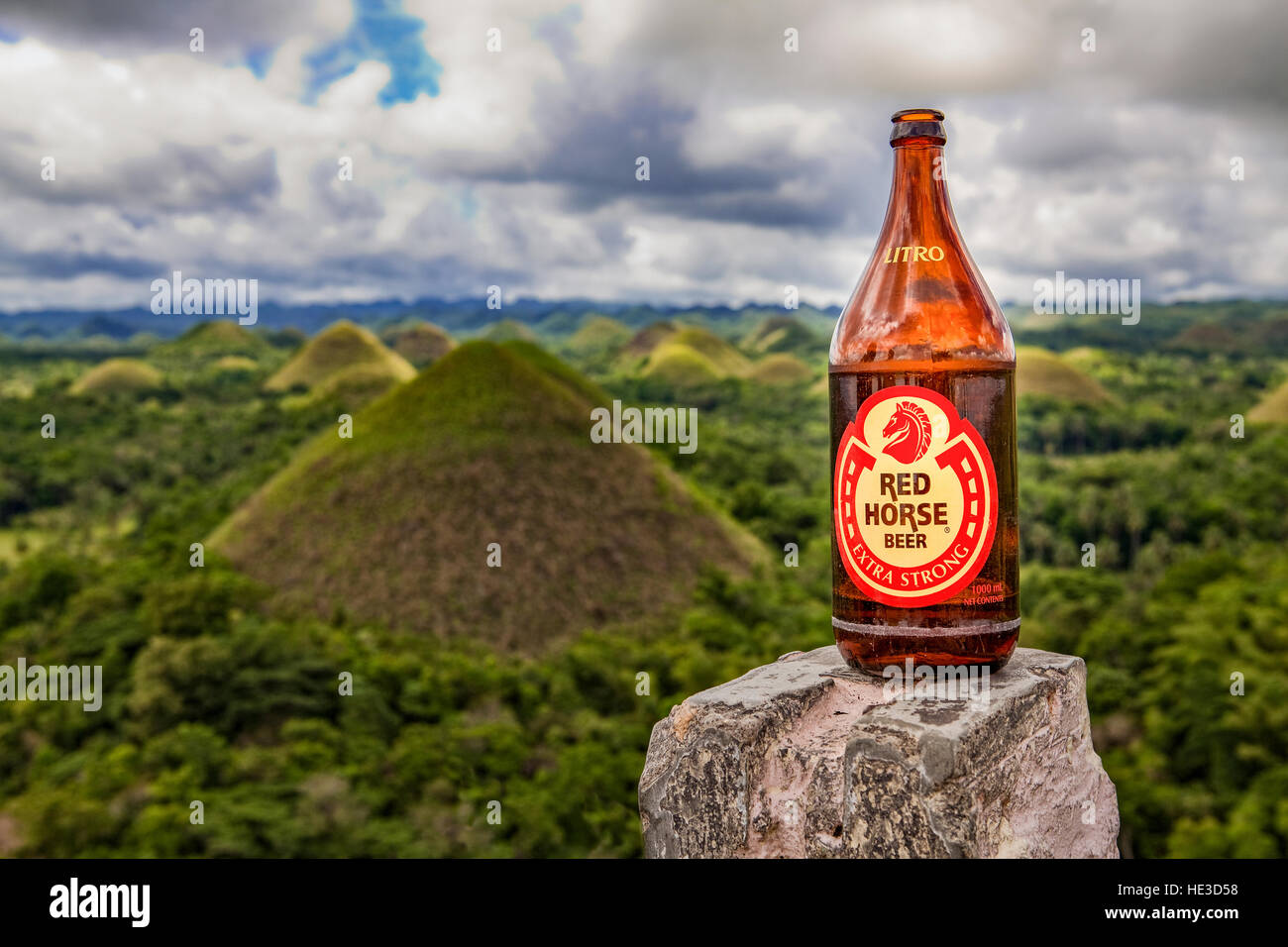 Una bottiglia da un litro di cavallo rosso Ale sorge su una roccia con il cioccolato colline di Bohol in background, Filippine. Foto Stock