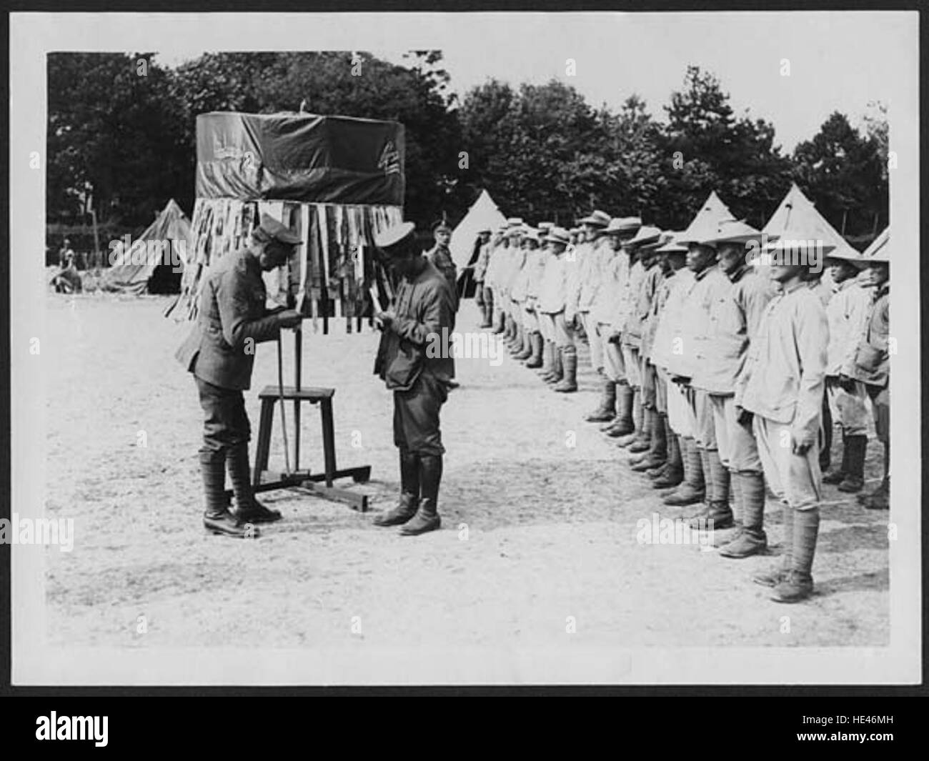 L'immagine raffigura una scena di un campo di lavoro cinese in Francia durante un'epoca passata, probabilmente all'inizio del XX secolo. Mostra che i lavoratori sono chiamati a appello nominale, una rappresentazione storica della vita dei campi di lavoro in quel periodo. Foto Stock