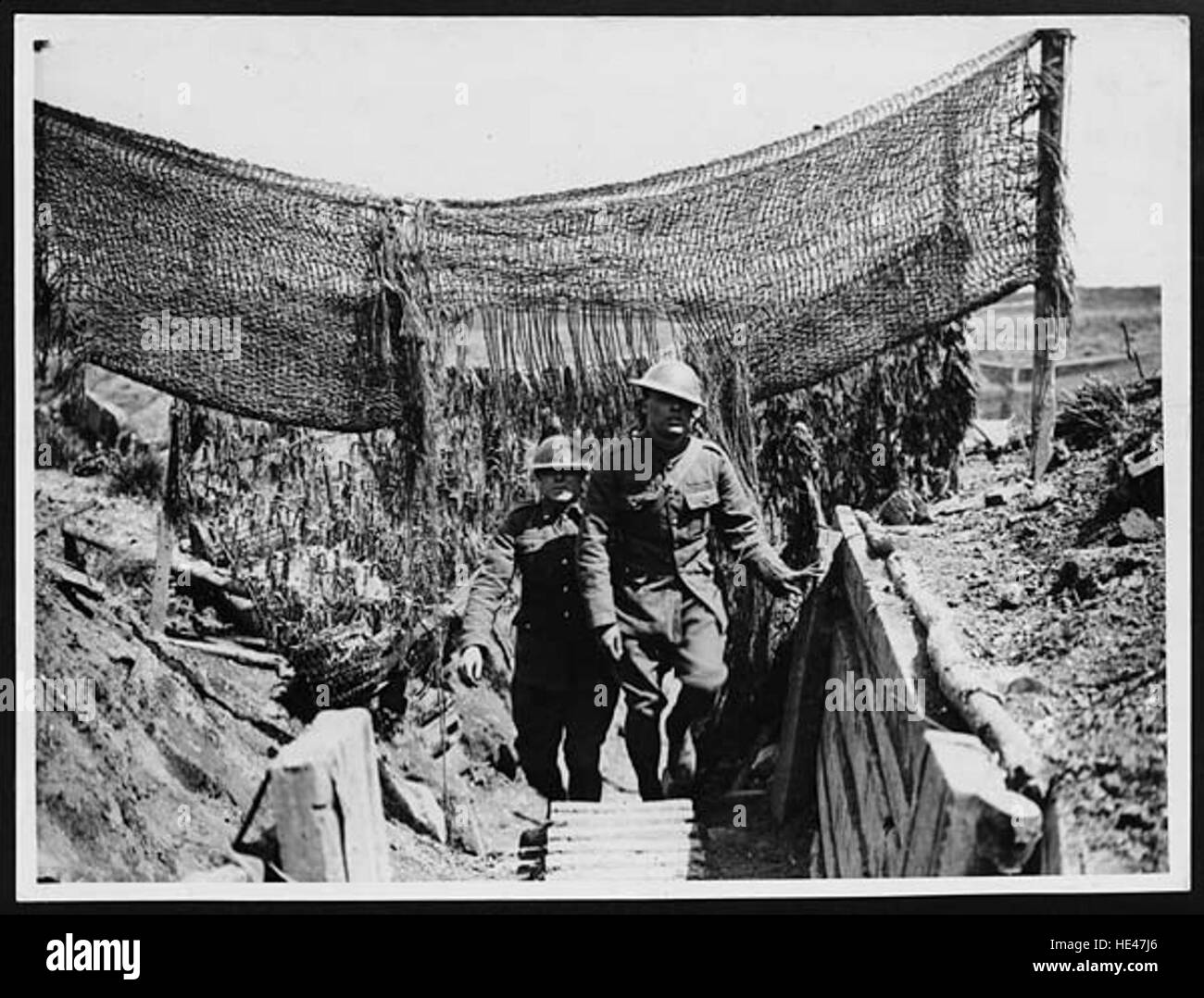 Questa immagine storica cattura i soldati che si muovono attraverso una trincea mimetica, parte di una strategia militare progettata per nascondere i movimenti e oscurare il rilevamento dei nemici. Riflette le tecniche di guerra tattica dei conflitti passati. Foto Stock