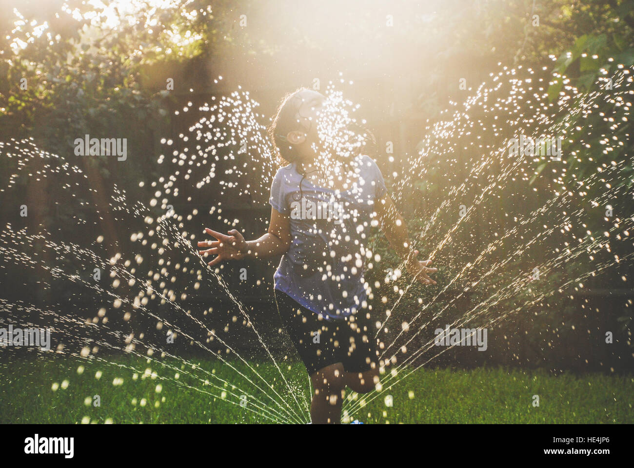 Ragazza che gioca in impianti sprinkler nella zona suburbana di backyard Foto Stock