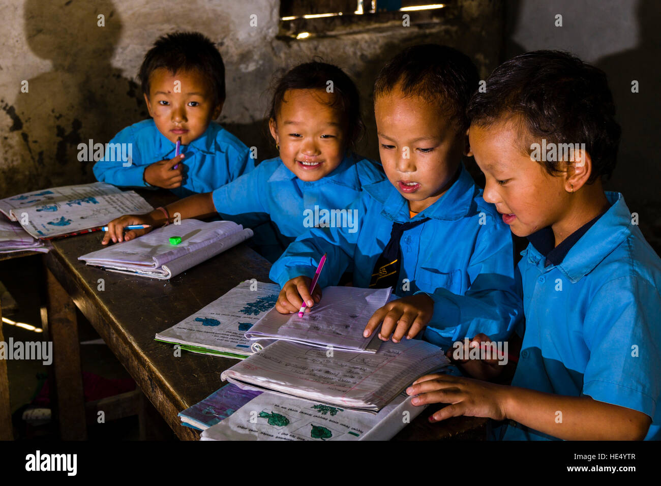 Un gruppo di bambini in abiti blu è seduto a un tavolo nella scuola locale, studiare Foto Stock