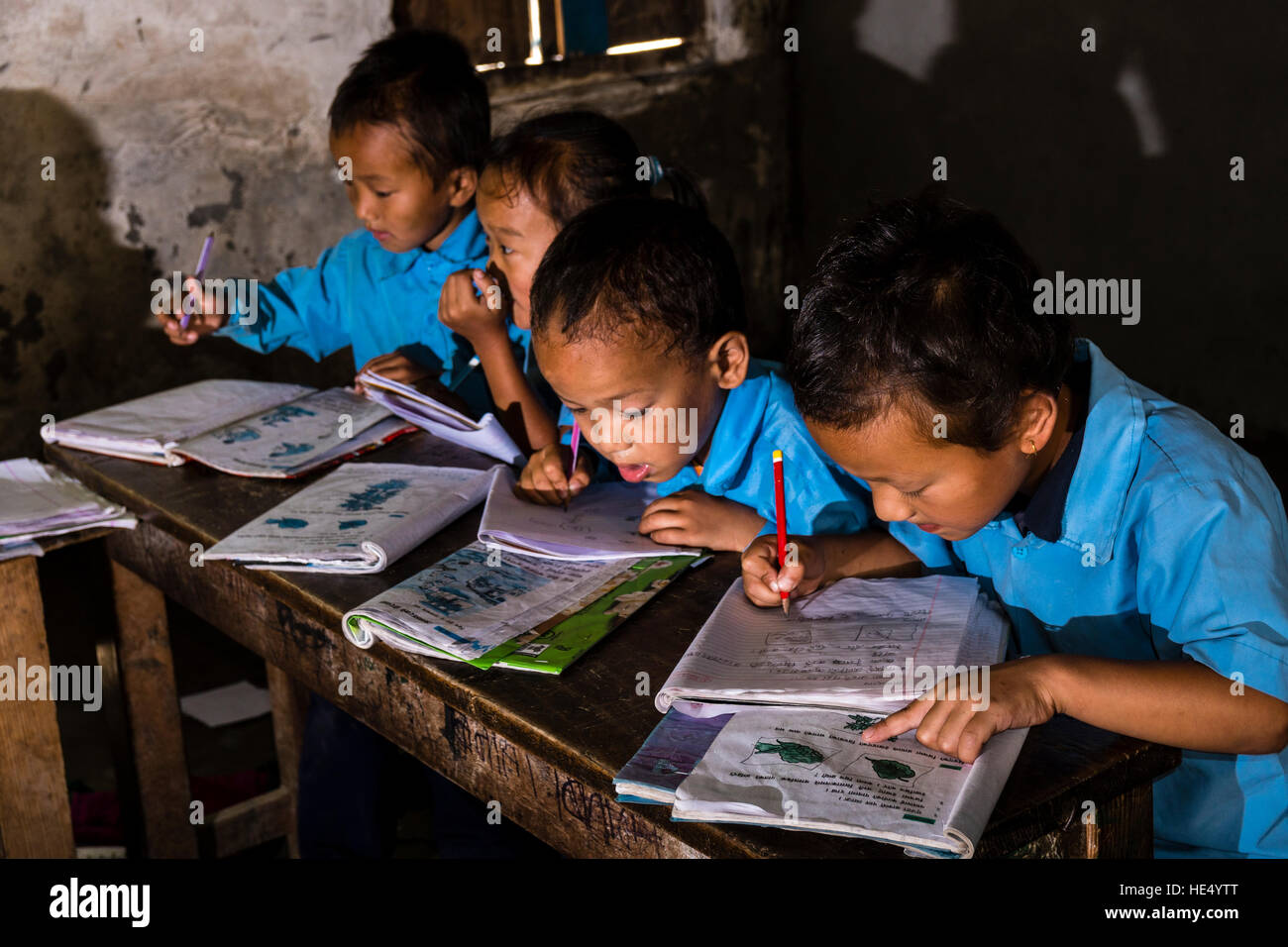 Un gruppo di bambini in abiti blu è seduto a un tavolo nella scuola locale, studiare Foto Stock