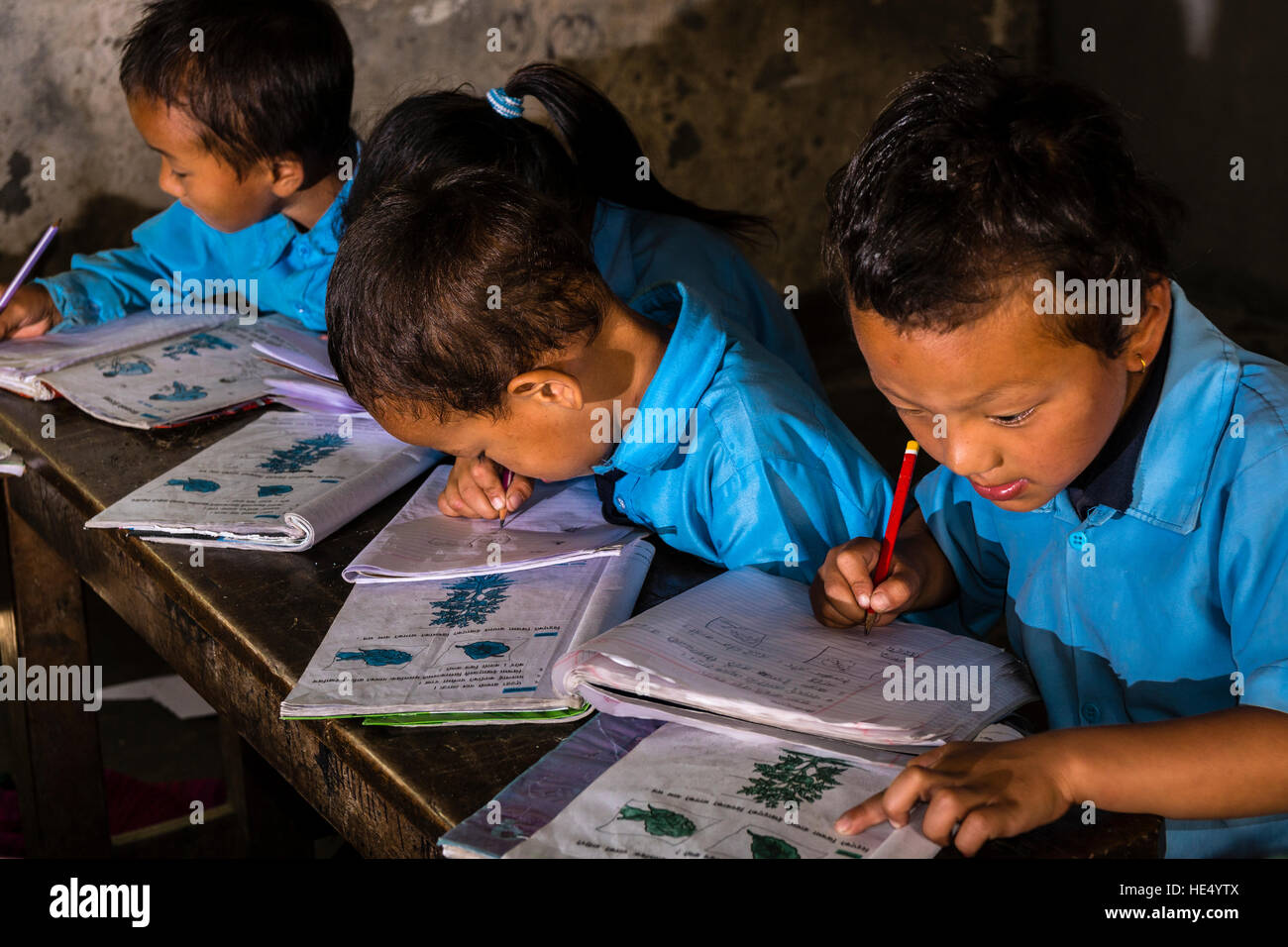 Un gruppo di bambini in abiti blu è seduto a un tavolo nella scuola locale, studiare Foto Stock