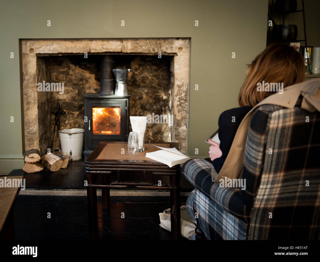 Donna accogliente leggendo un libro nella parte anteriore di un bruciatore di log che può essere vietata nel Regno Unito Foto Stock