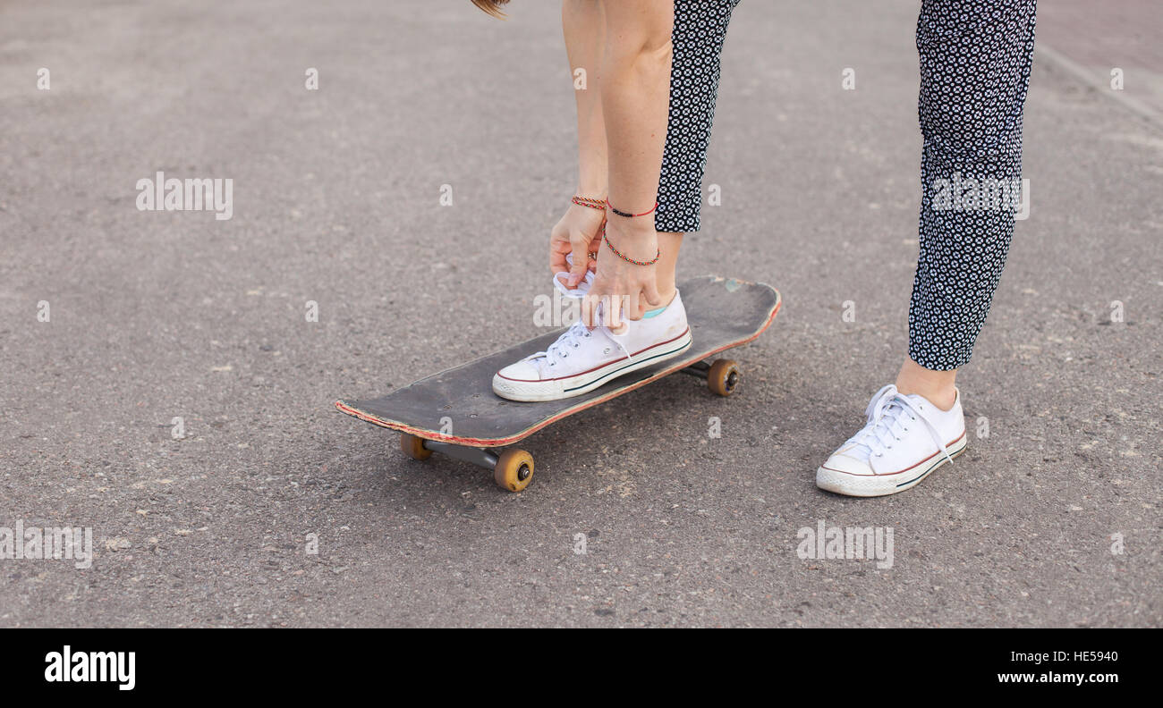 La donna sullo skateboard legatura di lacci delle scarpe Foto Stock