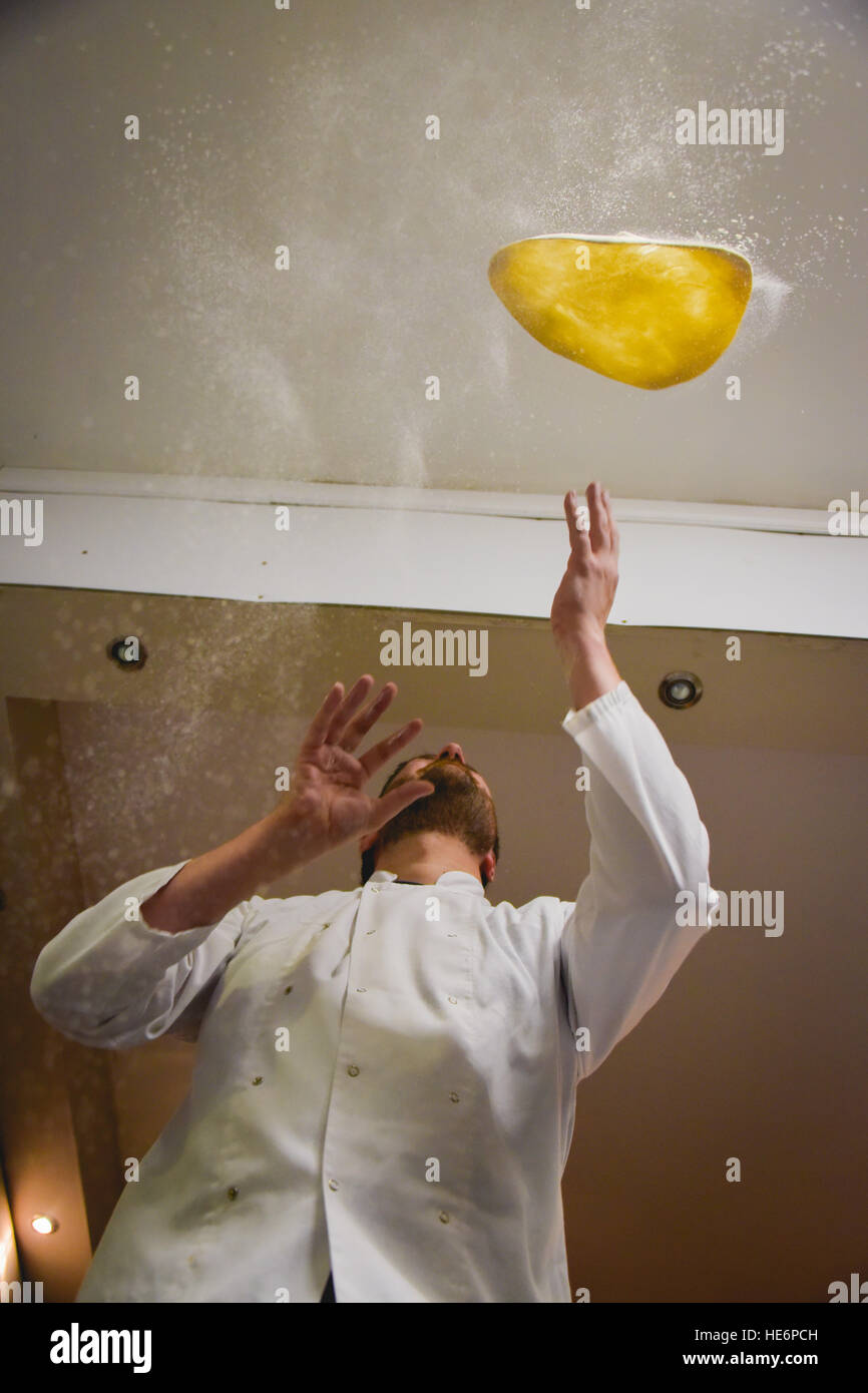 Lo Chef tossing pizza base in nuvole di polvere di farina Foto Stock