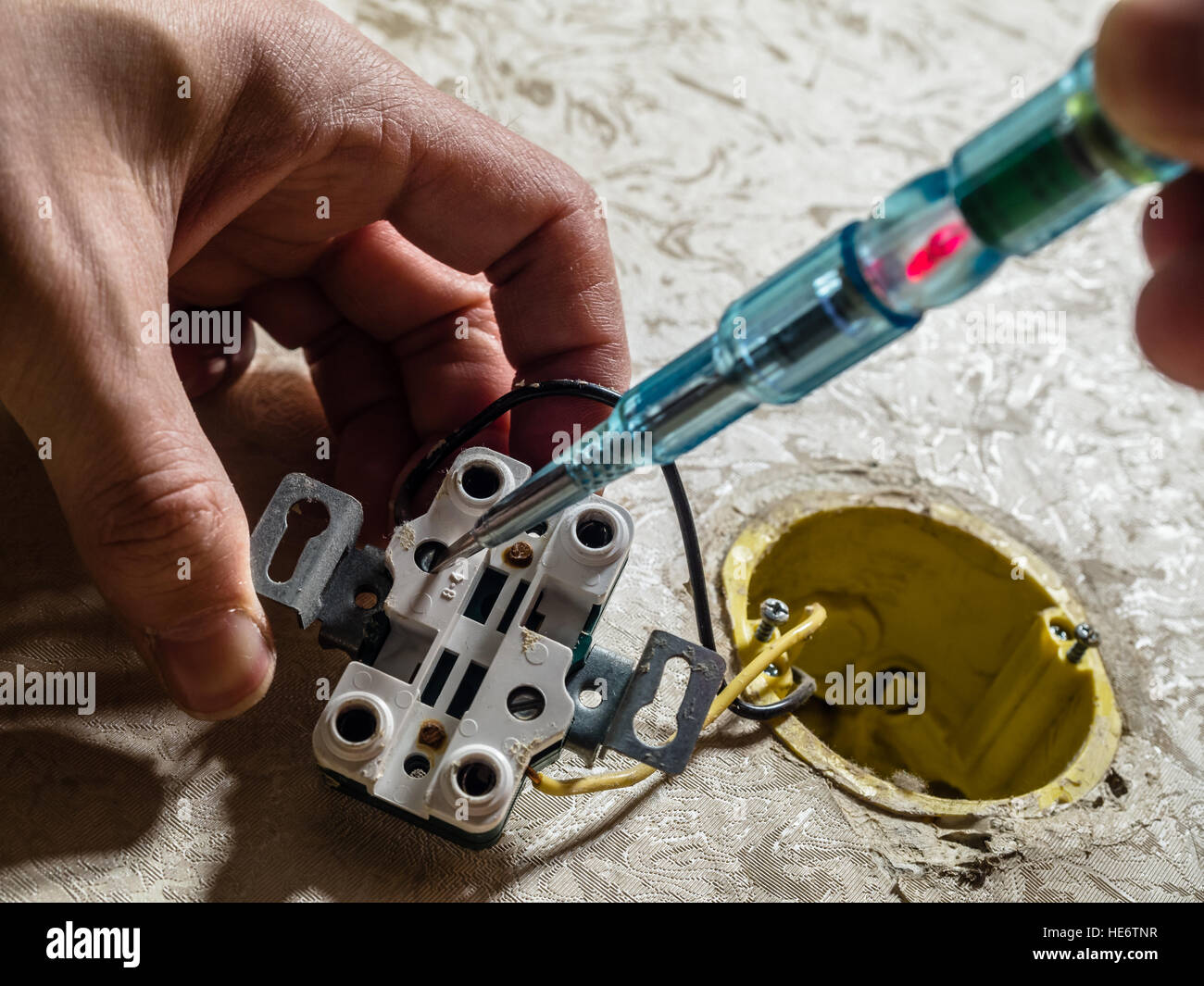 Mano che tiene un cacciavite punta verso un danneggiata presa elettrica. Foto Stock