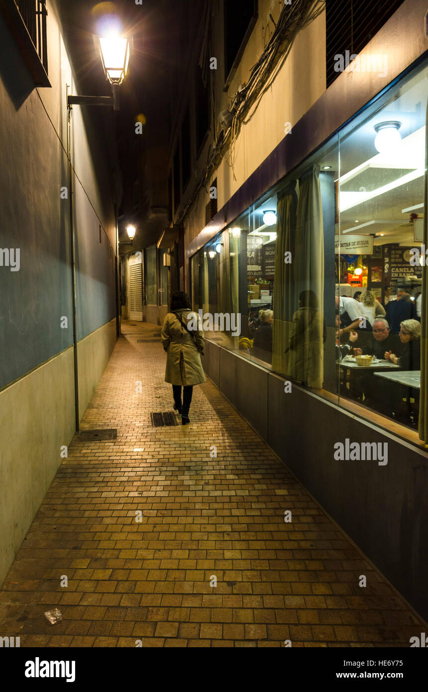 Donna cammina in condizioni di luce scarsa, stretto vicolo buio. Bar accanto ad essa. Spagna Foto Stock