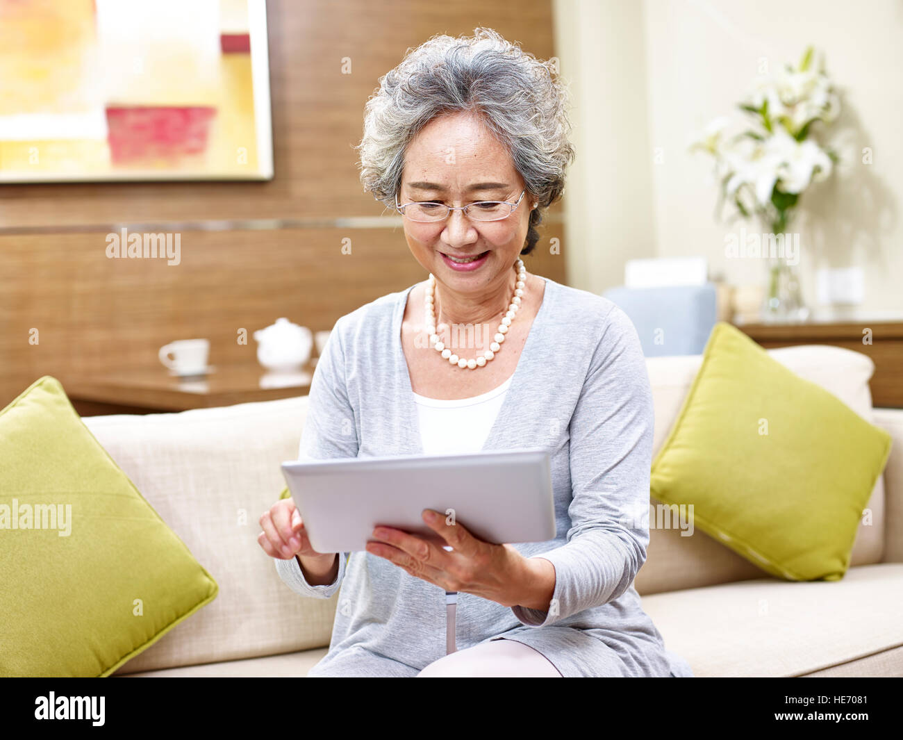 Senior donna asiatica seduto sul divano di casa utilizzando un computer tablet. Foto Stock