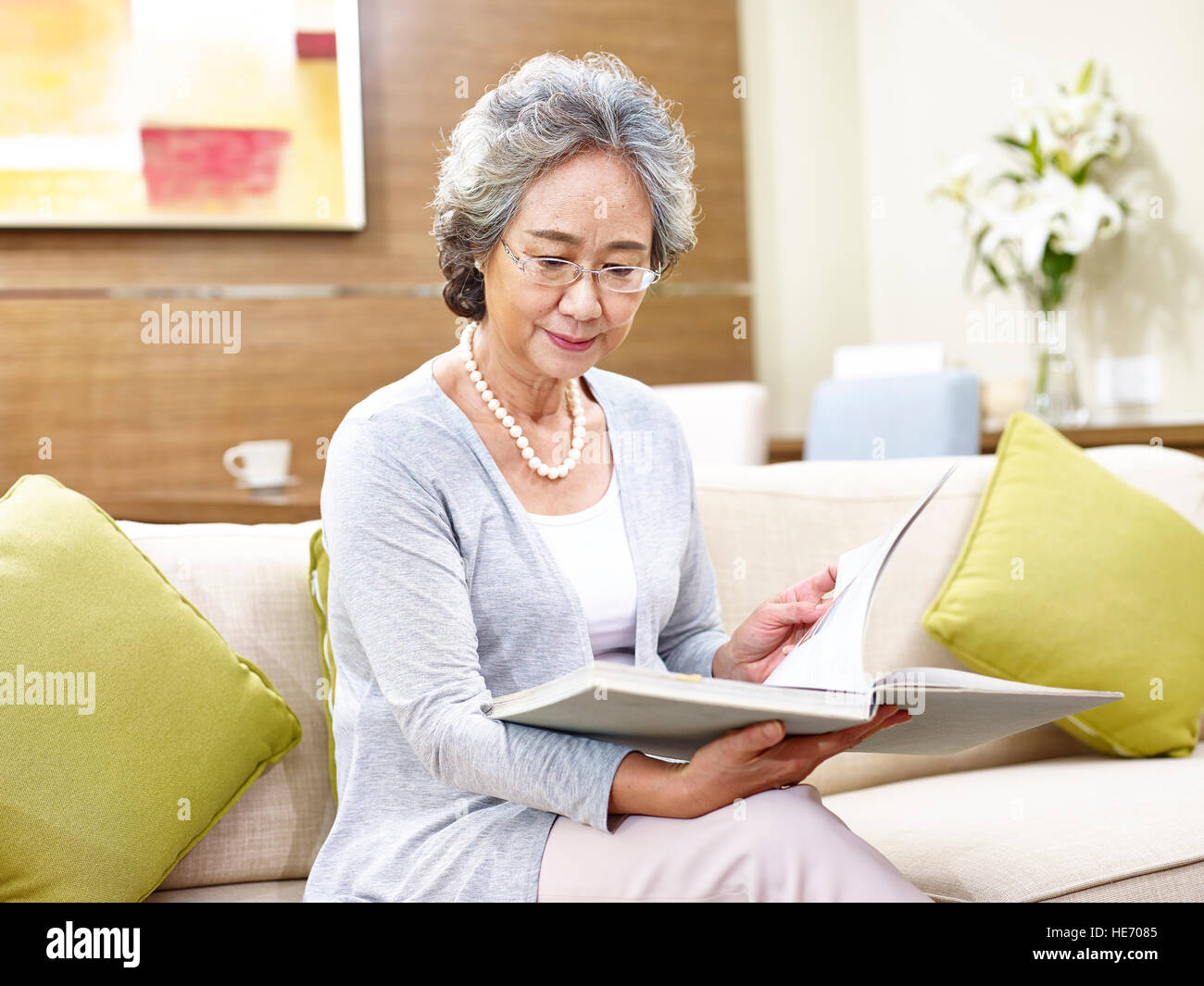 Senior donna asiatica seduto sul divano di casa a leggere un libro. Foto Stock