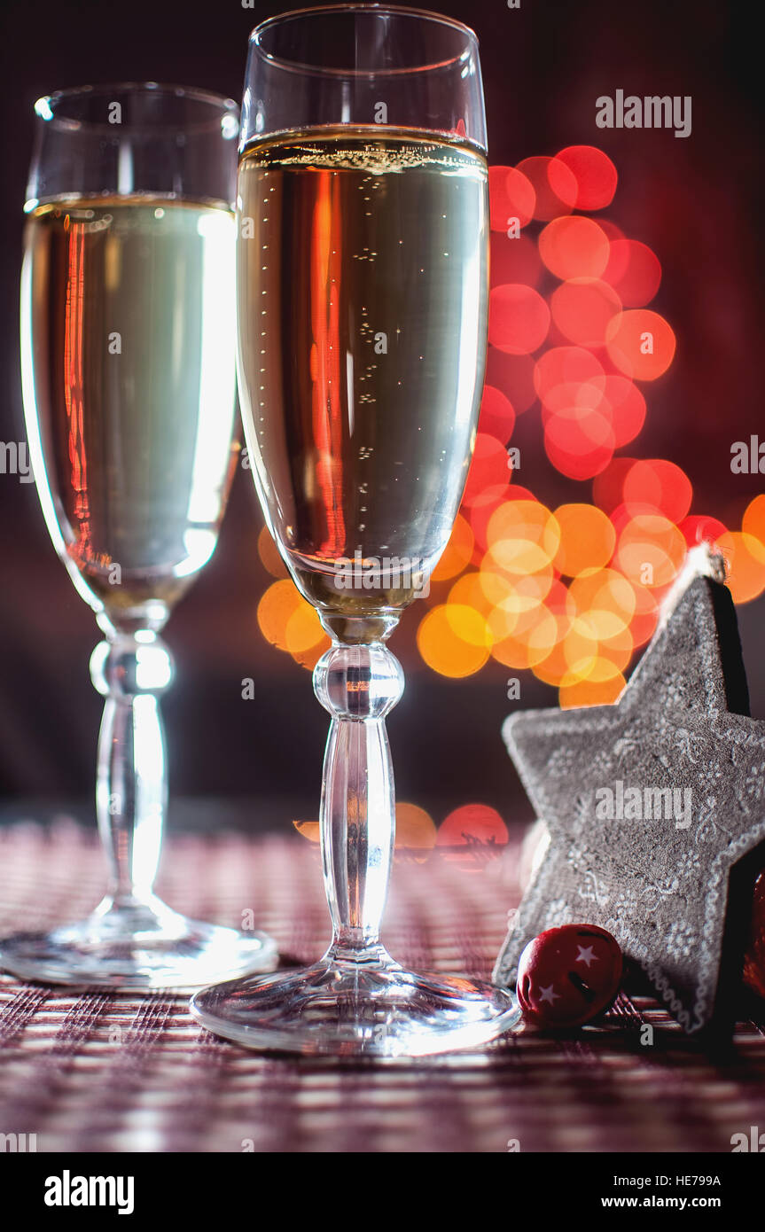 La vigilia di capodanno. Immagine di due wineglasses di champagne e legno decorativo stella sullo sfondo delle luci bokeh di fondo. Tasto basso. Messa a fuoco selettiva. Foto Stock