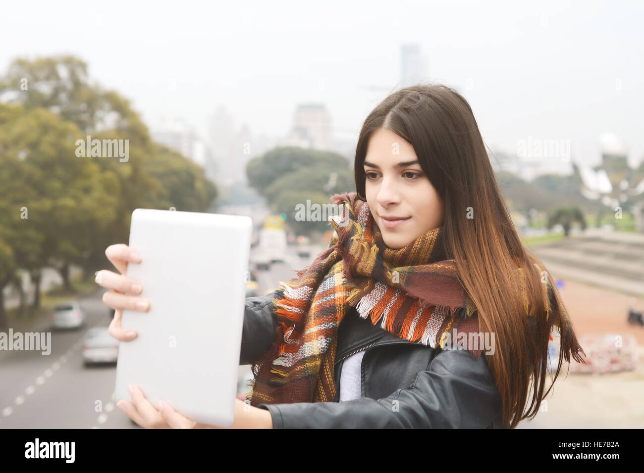 Ritratto di una giovane donna bellissima tenendo selfie con il suo tablet. All'esterno. Scena urbana. Foto Stock