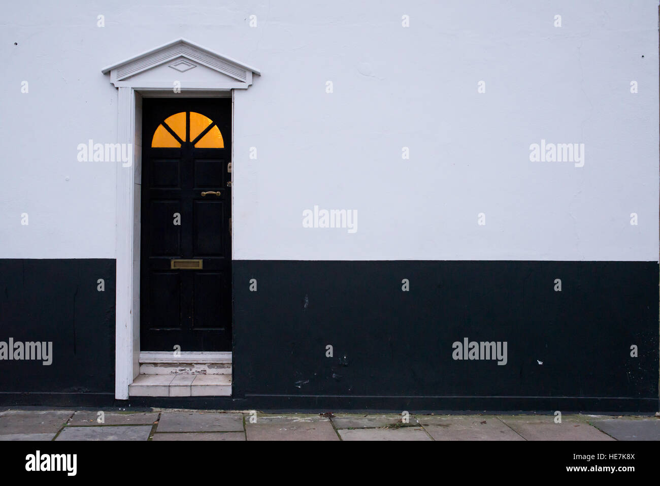 Legno nero porta in stile vittoriano su un bianco e nero parete con pannello di vetro sulla parte superiore e il caldo colore giallo luce proveniente dall'interno Foto Stock