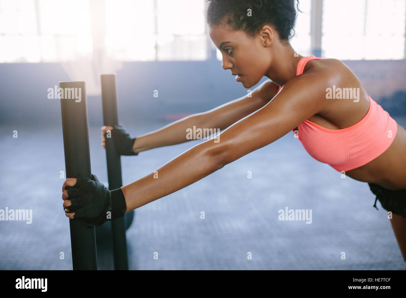 Vista laterale colpo di forte giovane donna spingendo la slitta in palestra. Donna africana facendo un intenso allenamento fisico in palestra. Foto Stock