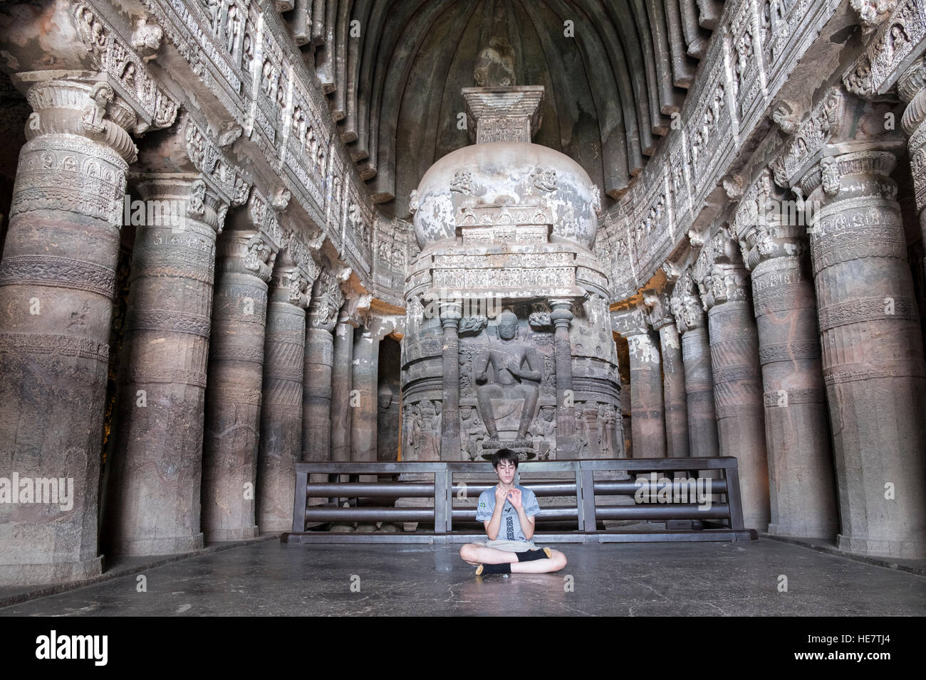 Un ragazzo che medita all'interno della Grotta 26 presso le grotte di Ajanta, patrimonio mondiale indù / buddista, Aurangabad, Maharashtra, India Foto Stock