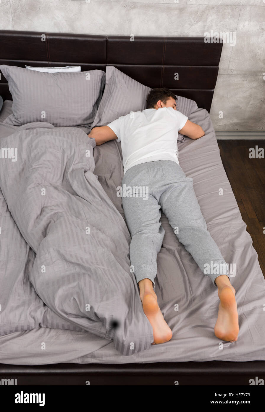 Giovane maschio stanco in pigiama dormire senza coperta in elegante bed in  sfumature di grigio e vicino al comodino con candele in una camera da letto  in stile loft Foto stock -